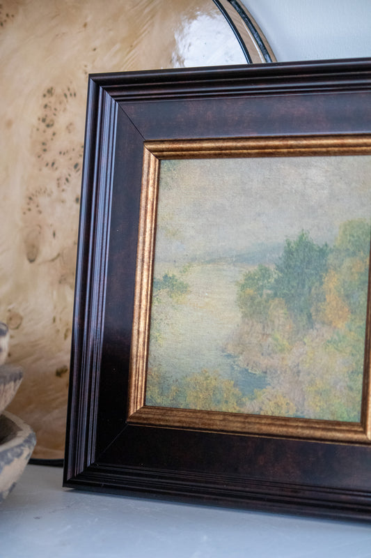 Framed painting of a landscape with trees and a body of water.