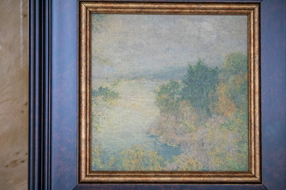 Framed painting of a landscape with trees and water on a blue wall.
