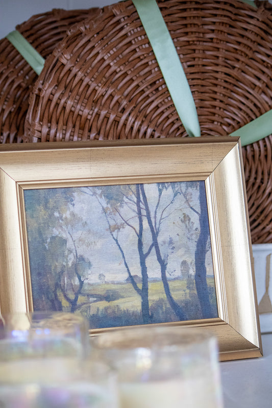 Framed landscape painting on a table with a woven basket in the background