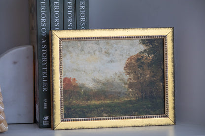 Framed landscape painting on a shelf with books in the background