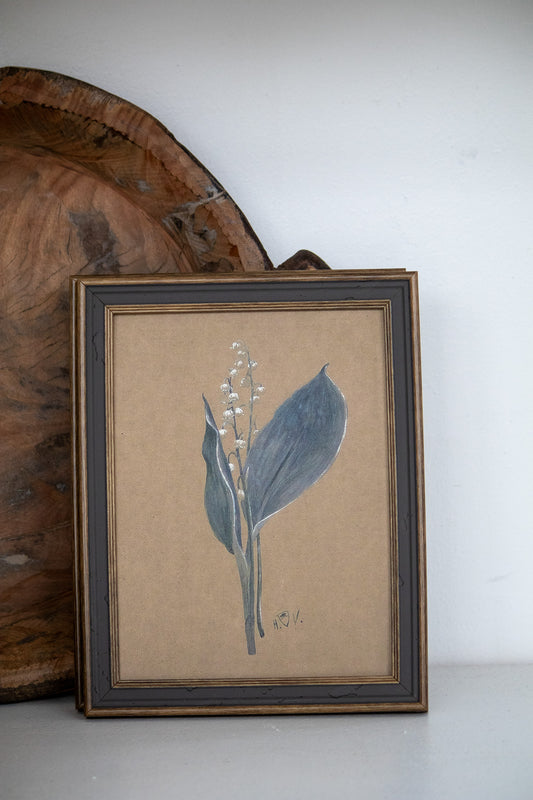 Framed botanical print of a leaf on a beige background, leaning against a wooden surface.