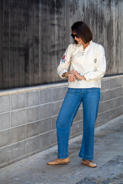 Woman wearing a white top and blue jeans standing against a gray wall.