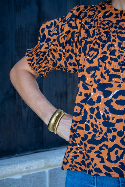 Person wearing an orange and black leopard print top with a blurred background