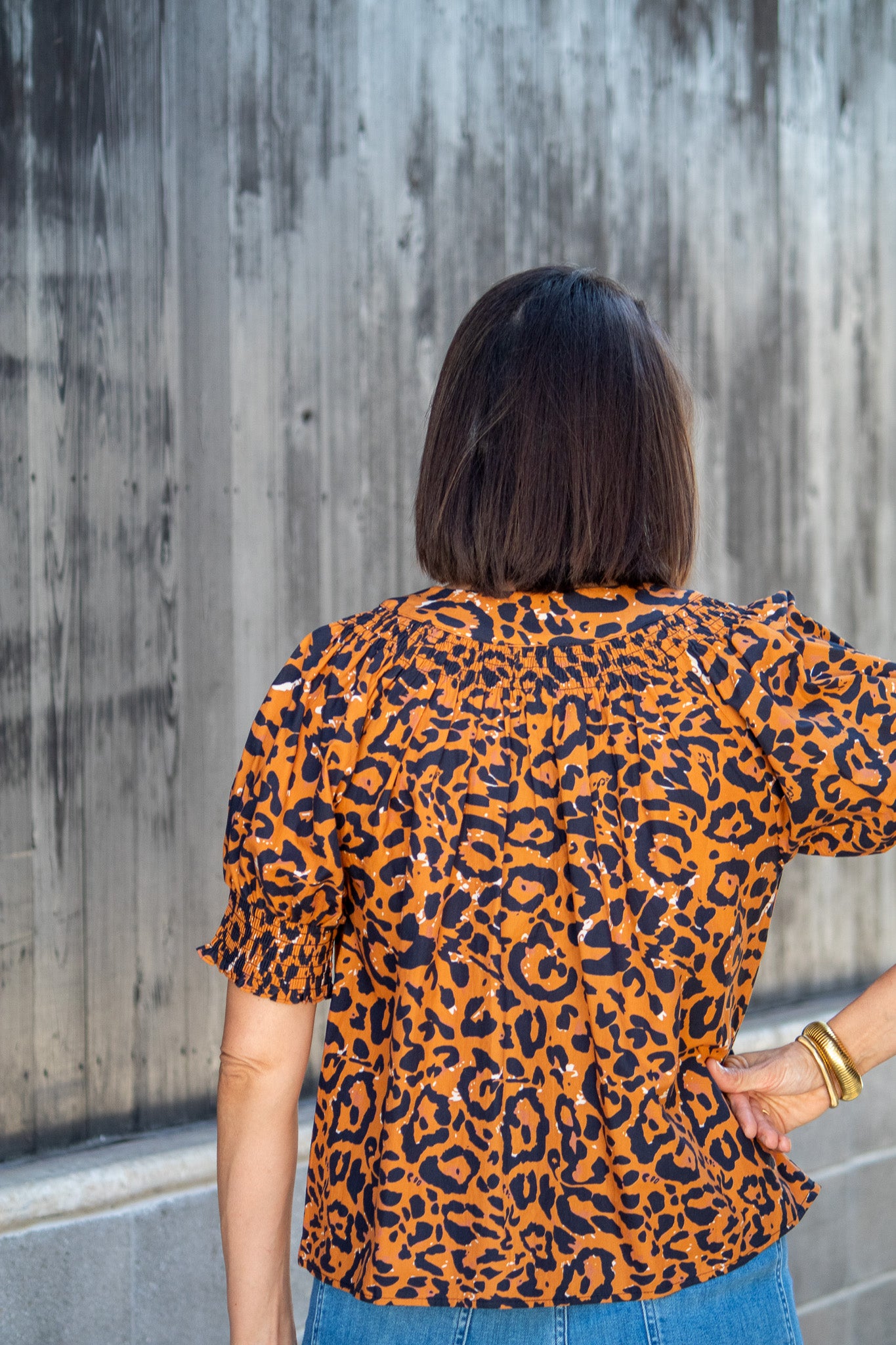Person wearing an orange and black leopard print top against a concrete wall.