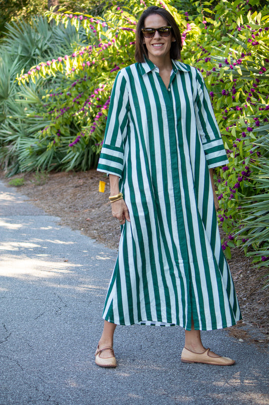 Woman wearing a green and white striped dress standing outdoors with plants in the background