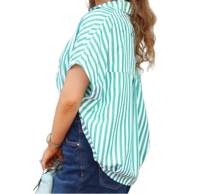 Woman wearing a green and white striped shirt and denim shorts standing outdoors.