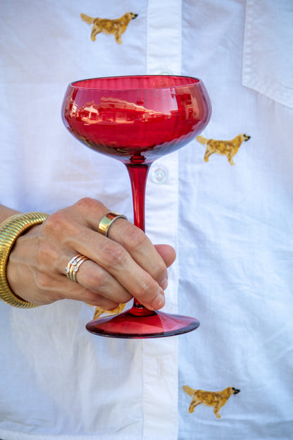 Red glass held by a hand with gold bangles against a white shirt with dog prints