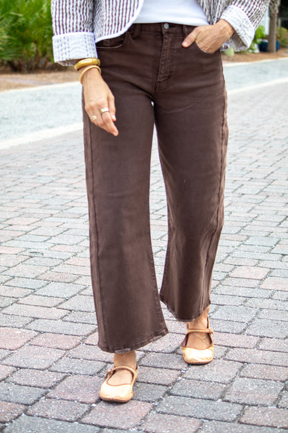 Person wearing brown wide-leg pants on a paved street.