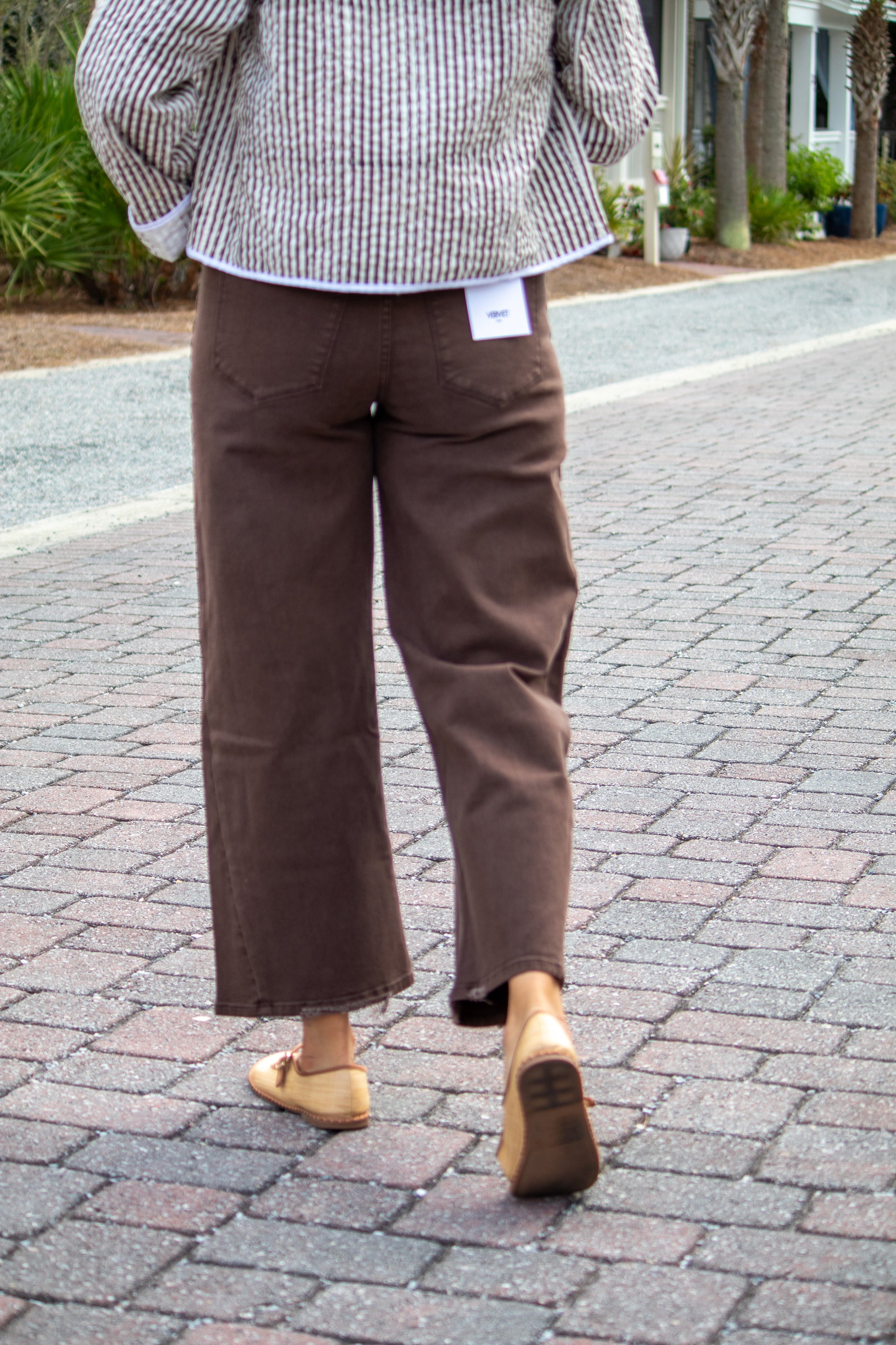 Person wearing brown pants and a checkered shirt on a paved walkway.