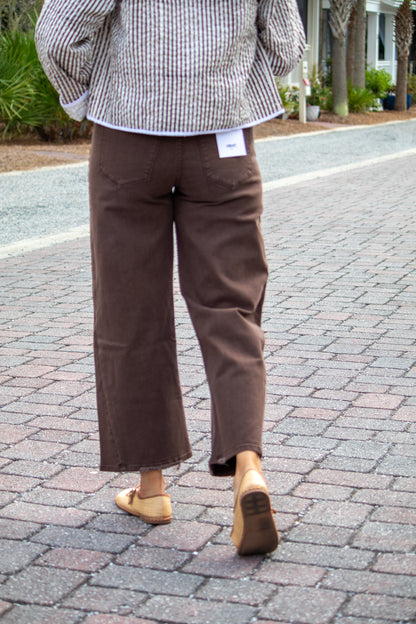Person wearing brown pants and a checkered shirt on a paved walkway.