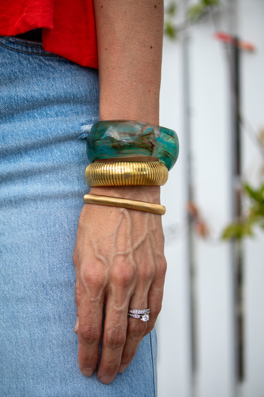Hand wearing gold and green bangles with a blurred background