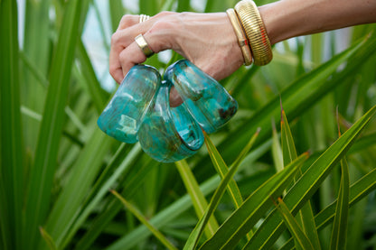 Hand holding three green bangles against a green leafy background