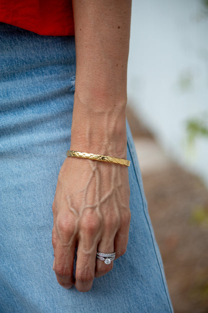 Close-up of a person's wrist wearing a gold bracelet and ring, with a blurred background.