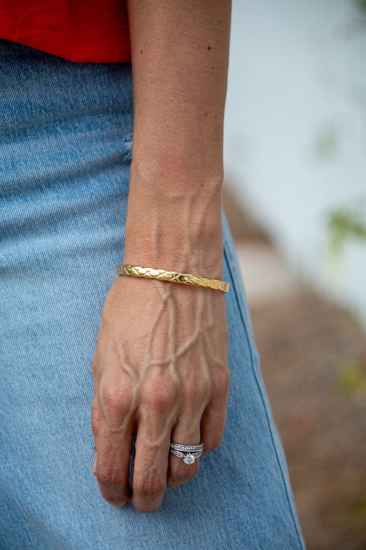 Close-up of a person's wrist wearing a gold bracelet and ring, with a blurred background.