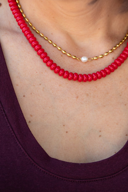 Red beaded necklace with a gold chain on a person wearing a purple top.