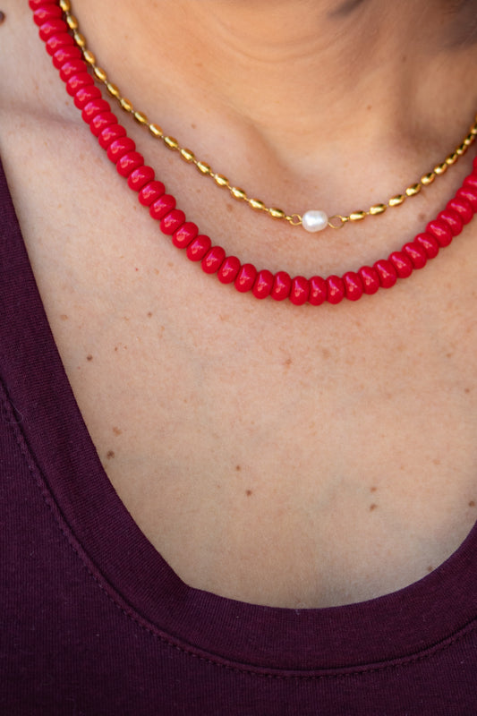 Red beaded necklace with a gold chain on a person wearing a purple top.