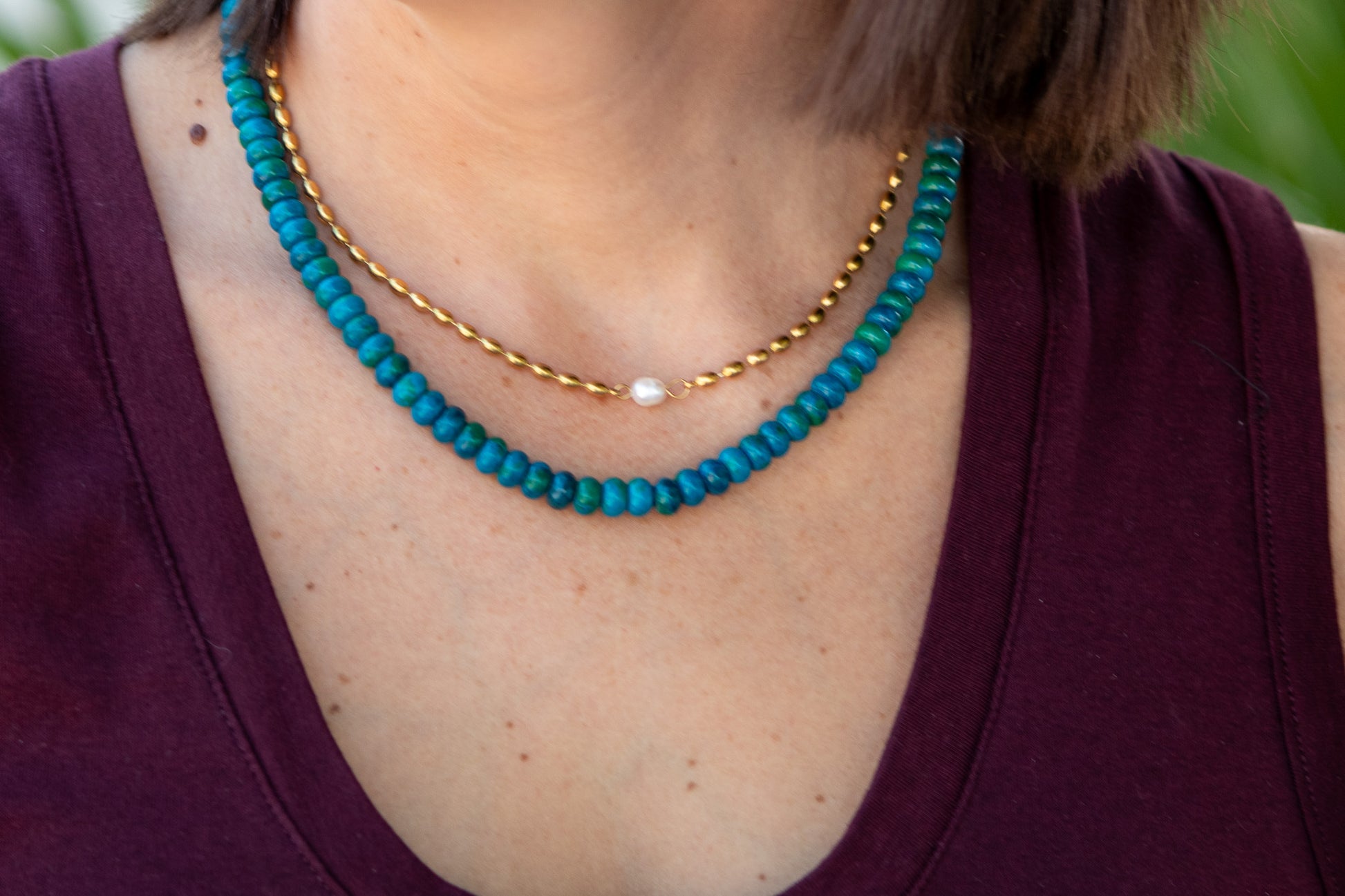 Close-up of a person wearing a turquoise beaded necklace with a gold chain.