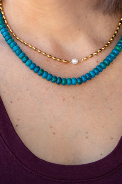 Close-up of a person wearing two necklaces: one turquoise beaded and one gold chain.