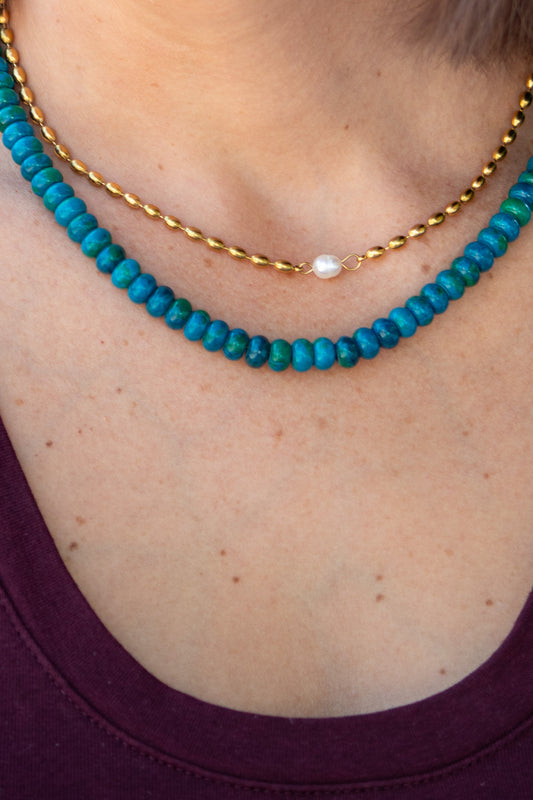 Close-up of a person wearing two necklaces: one turquoise beaded and one gold chain.