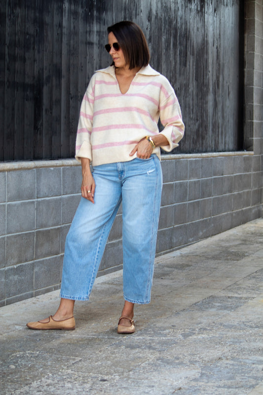 Woman wearing a striped sweater and jeans standing against a gray wall.