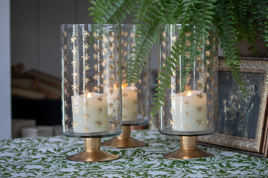 Decorative candle holders with gold star patterns on a table with a plant in the background.