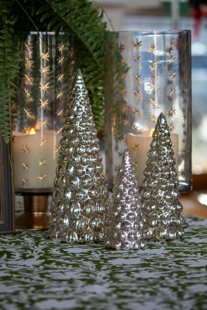 Decorative silver Christmas trees in front of glass candle holders with star patterns.