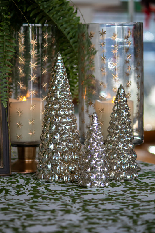 Decorative silver Christmas trees in front of glass candle holders with star patterns.