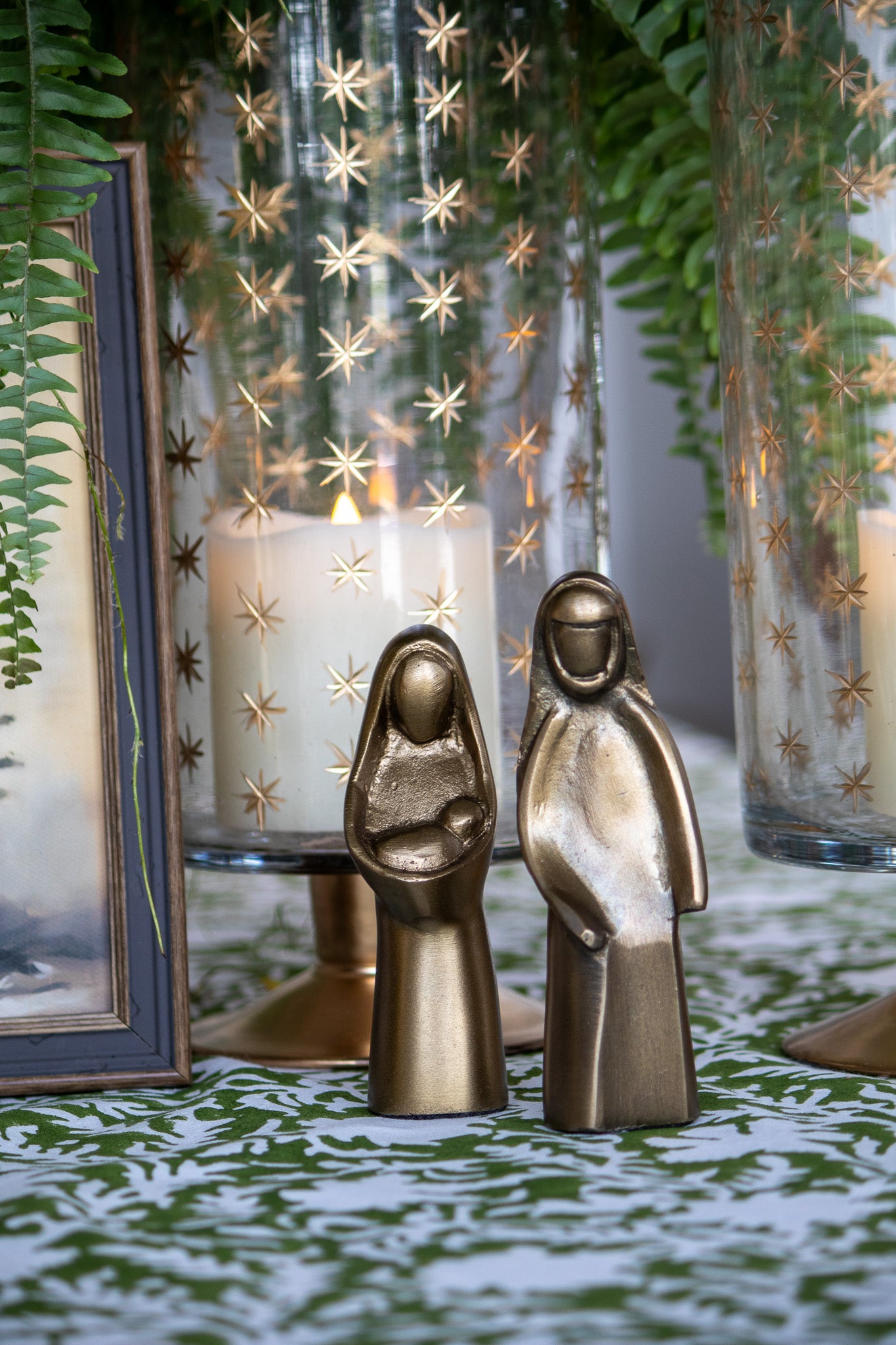 Bronze nativity scene figures with candles and decorative lanterns in the background.