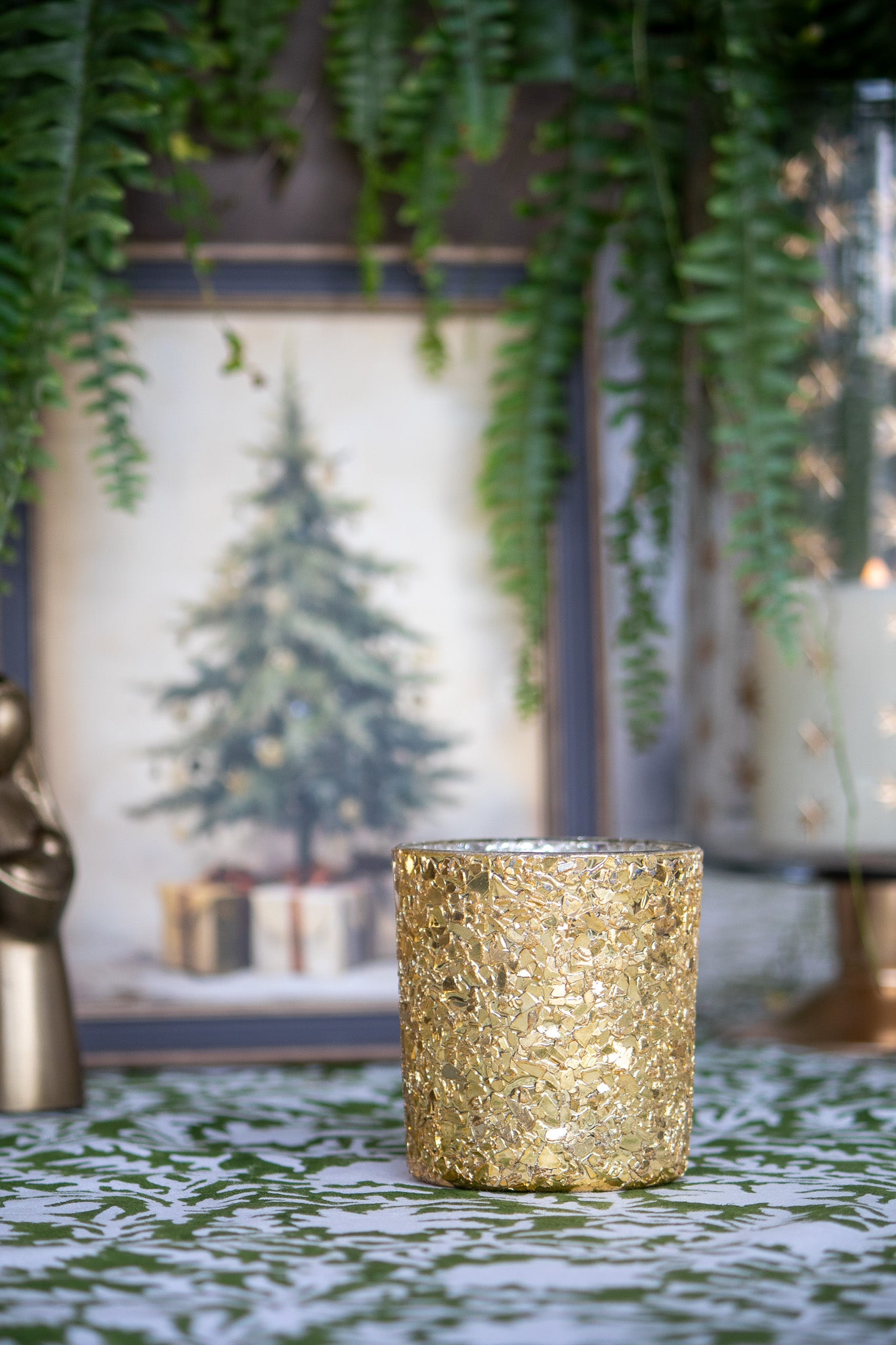 Gold glittery candles  on a decorative surface with plants and framed picture in the background