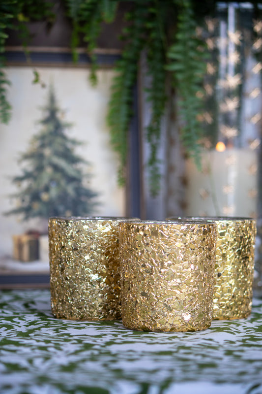 Three gold glittery candles on a table with a blurred festive background.
