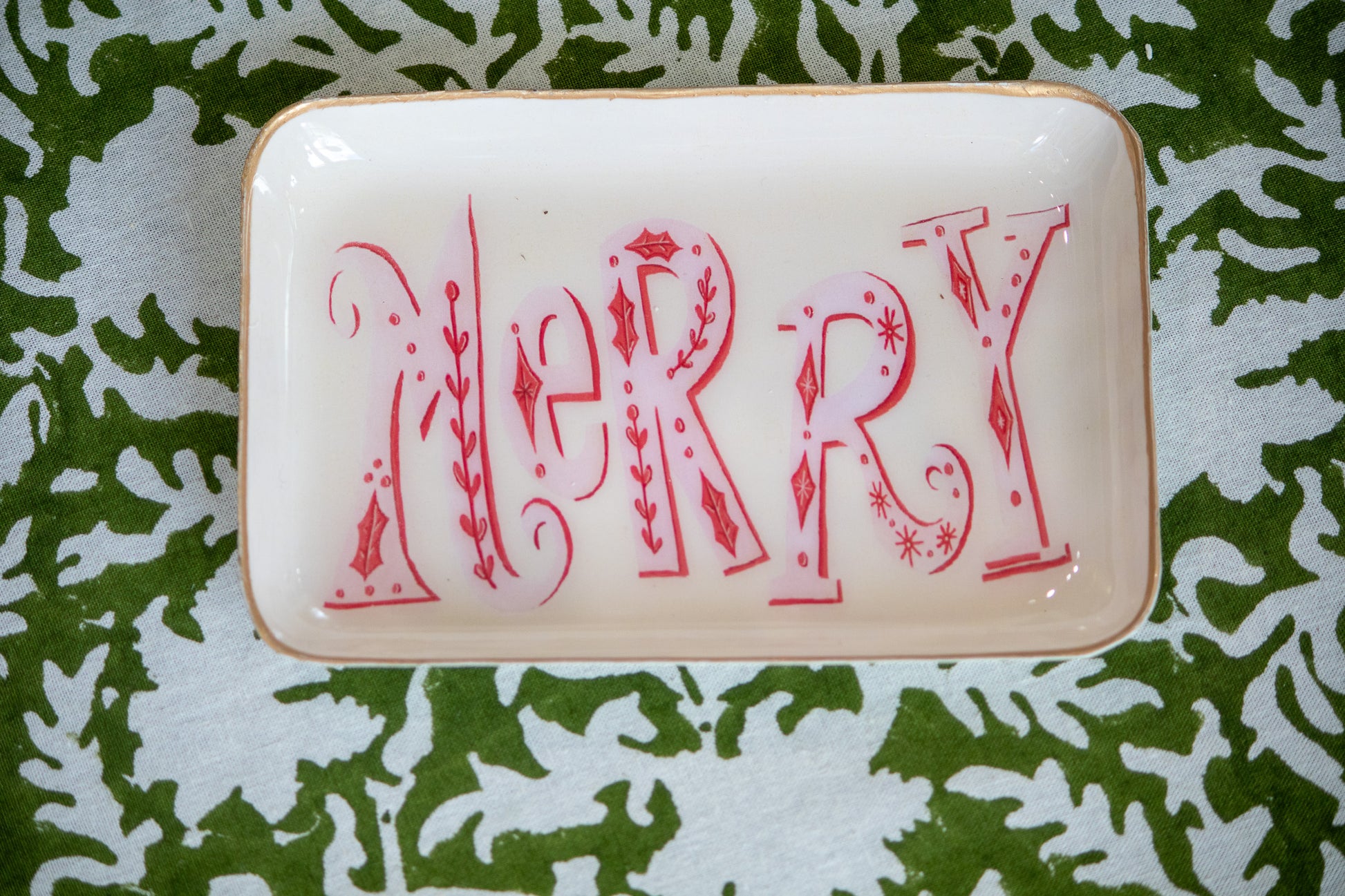 Decorative tray with 'MERRY' in red letters sitting on green and white patterned table cloth 