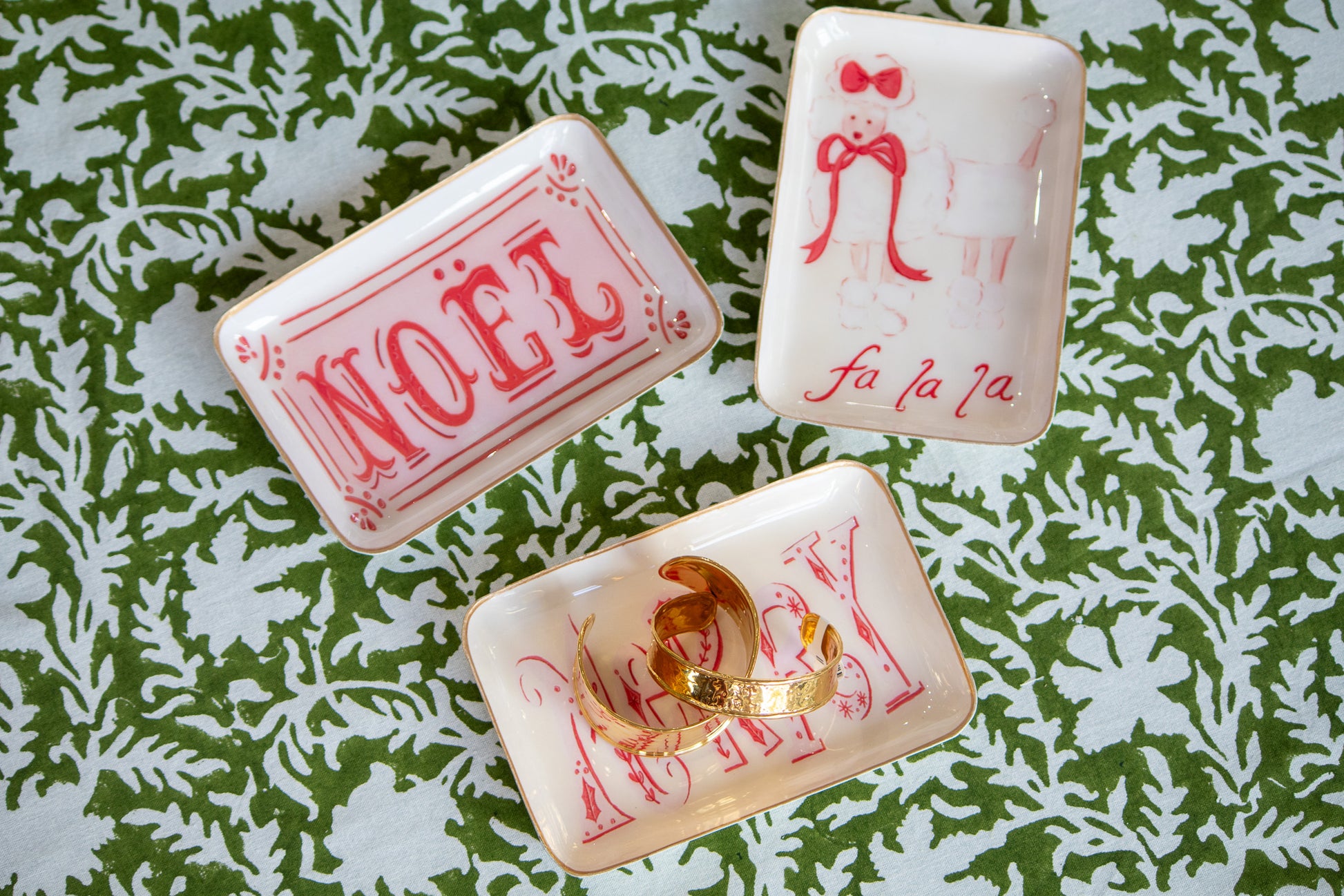 Three decorative metal trays  with festive designs on a green and white patterned surface.