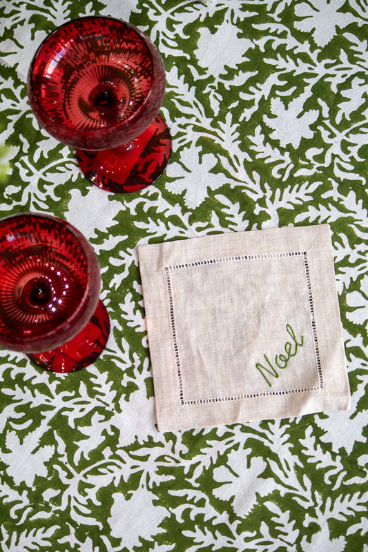 Coaster with 'Noel' text on a green and white patterned tablecloth with red glassware.
