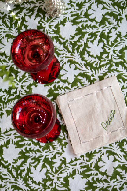 Red glassware and a beige coaster with 'Peace' on a green and white patterned tablecloth.