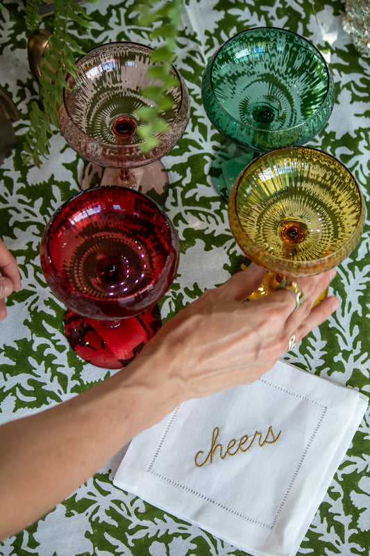 Colorful glassware on a table with a 'cheers' napkin.
