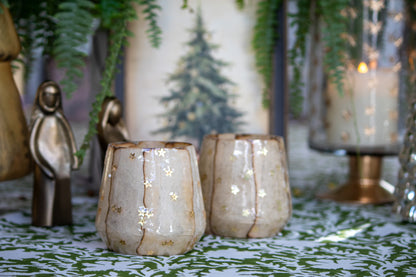 Decorative candles in ceramic holders on a patterned surface with greenery in the background