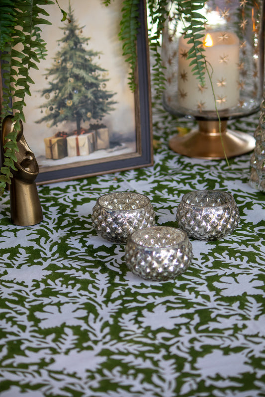 Decorative table setting with silver candle holders, a Christmas-themed painting, and a lit candle.