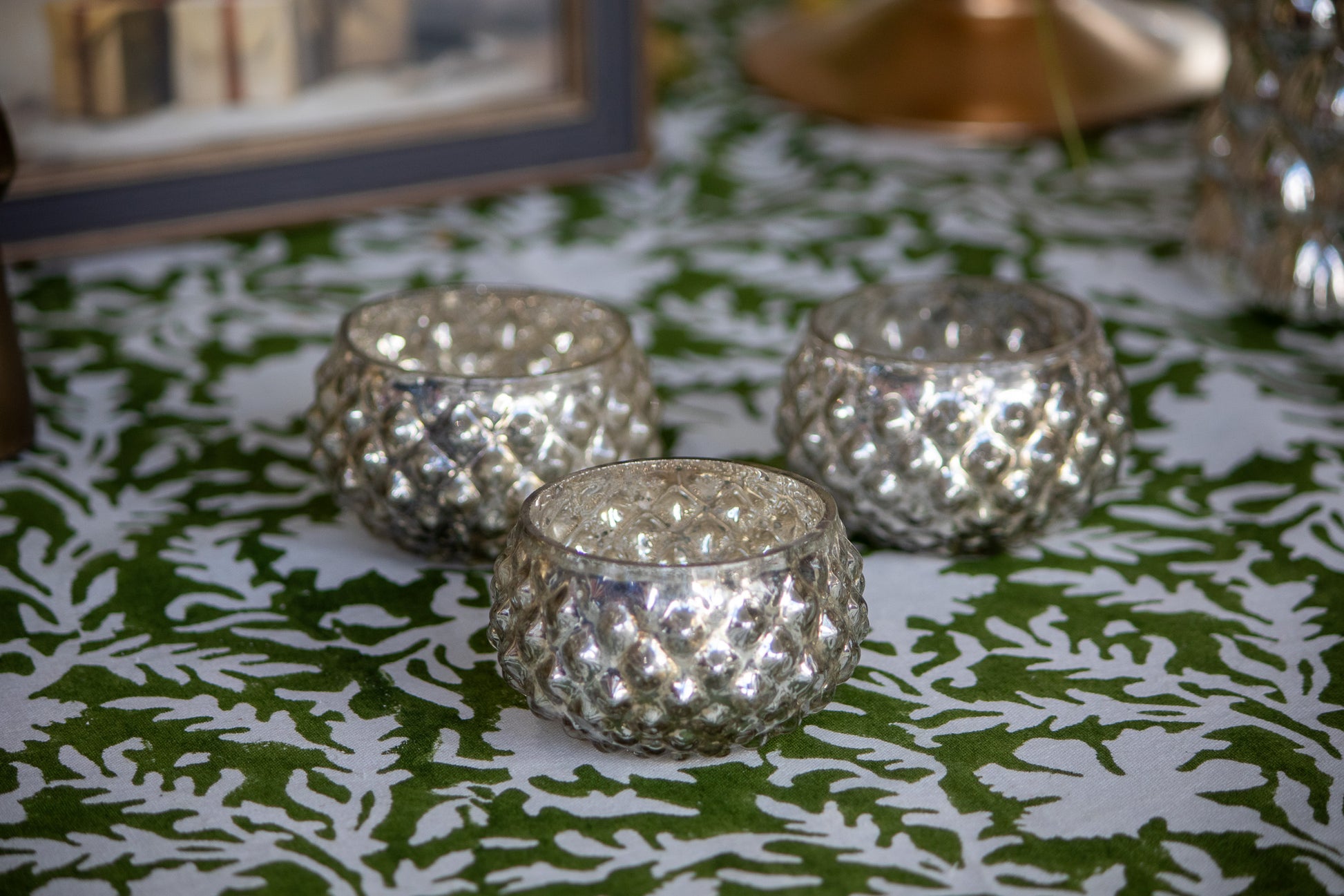 Three silver textured candle holders on a green and white patterned tablecloth.