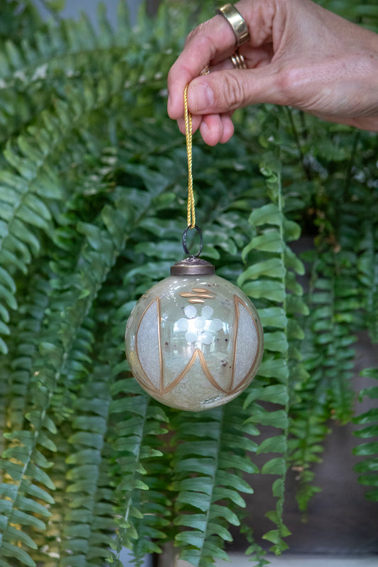 Decorative glass ornament with gold accents hanging from a hand against a fern background