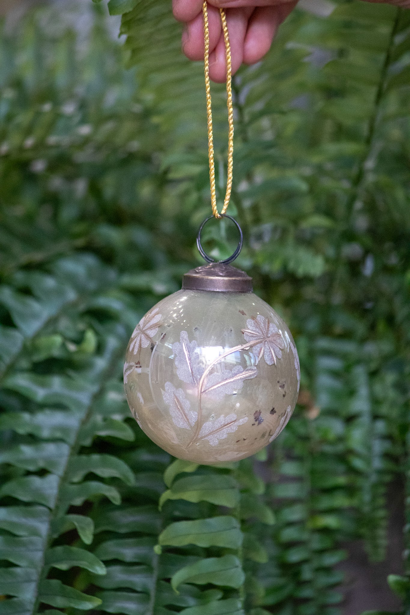 Decorative glass ornament with floral patterns hanging against a fern background