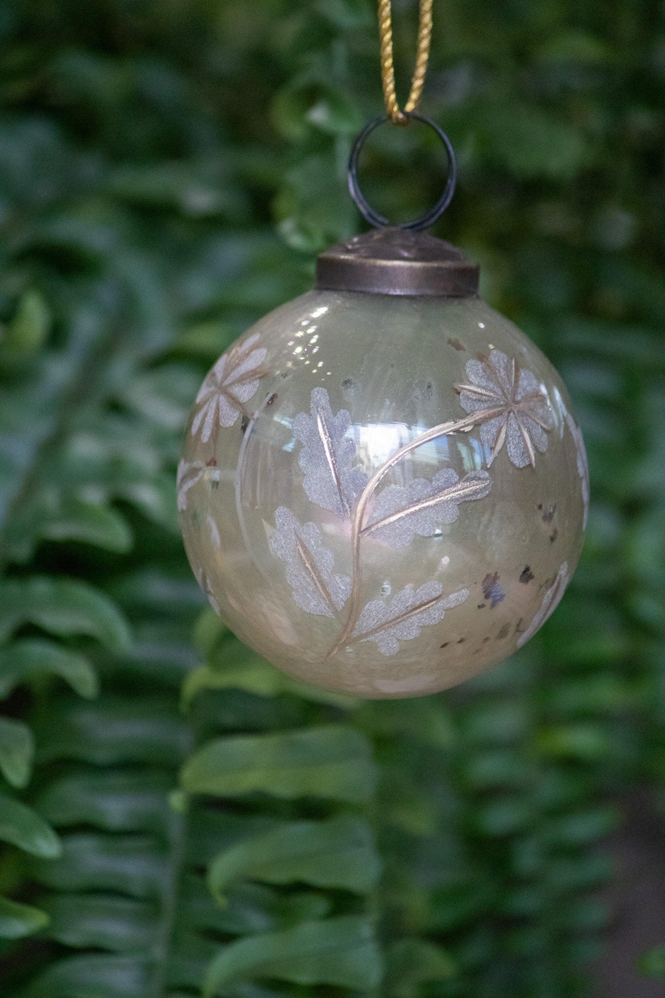 Decorative glass ornament with floral patterns hanging against a green leafy background