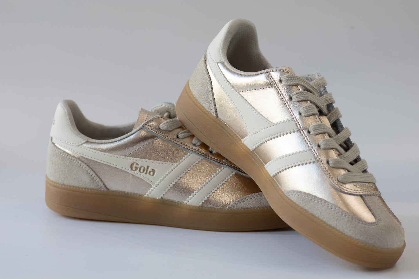 Pair of Gola sneakers with beige and metallic  color scheme on a light gray background