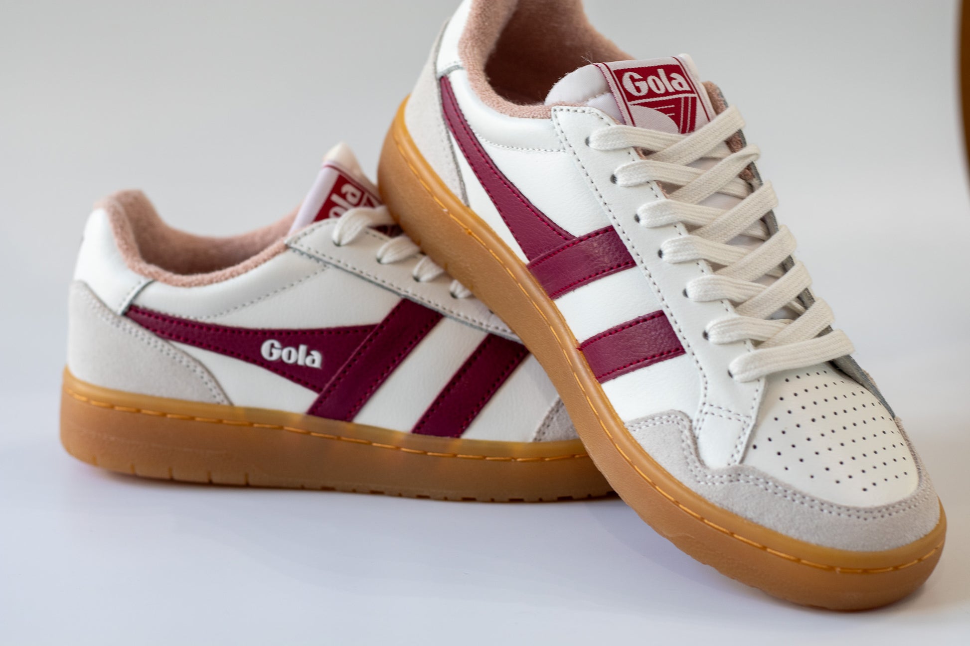White sneakers with maroon stripes and 'Gola' branding on a light gray background