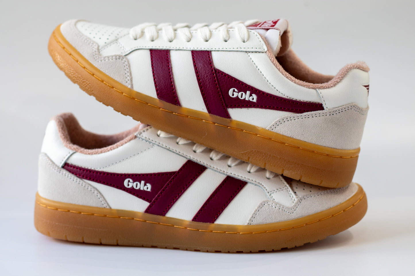 White sneakers with maroon stripes and brown soles on a light gray background
