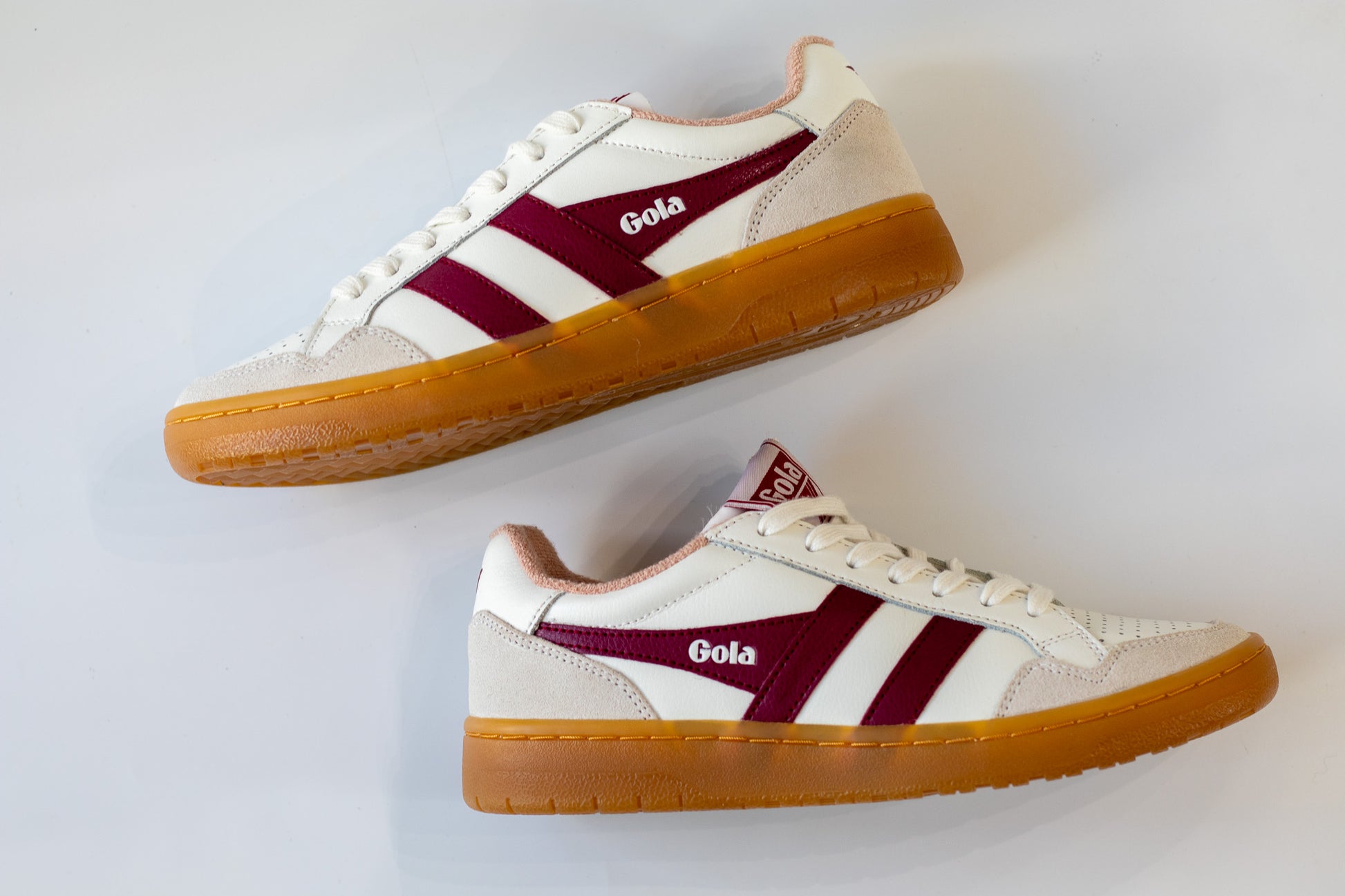 Pair of white sneakers with maroon accents and brown soles on a light gray background