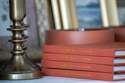 Stack of red books with gold text next to brass candlesticks on a blurred background