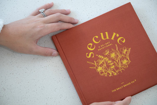 Red book titled 'secure' with yellow text and floral design on a white surface, held by a hand.