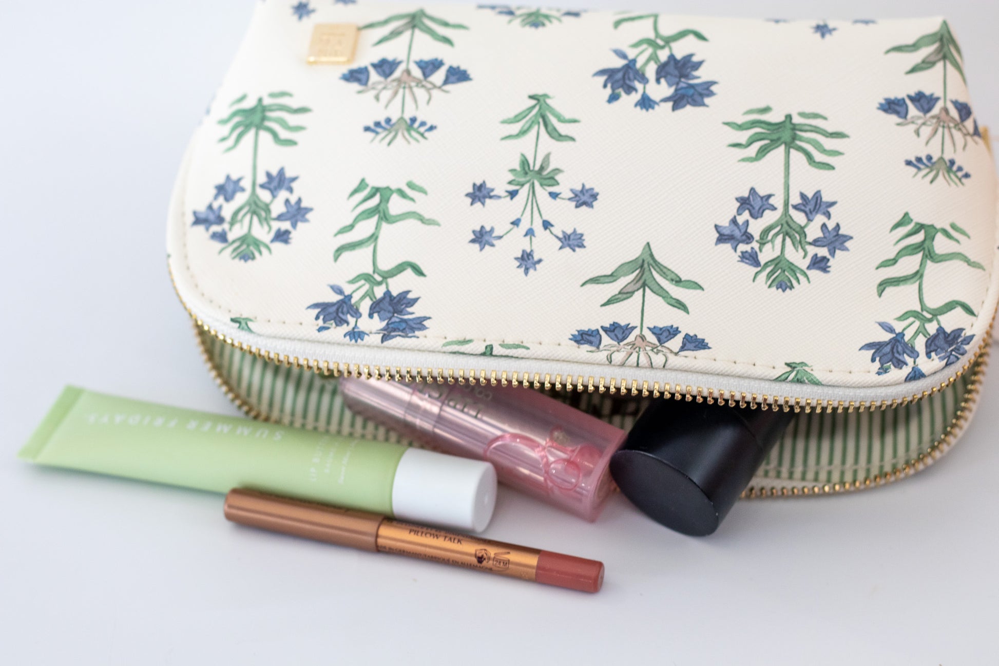 Makeup pouch with floral pattern containing makeup items on a white background