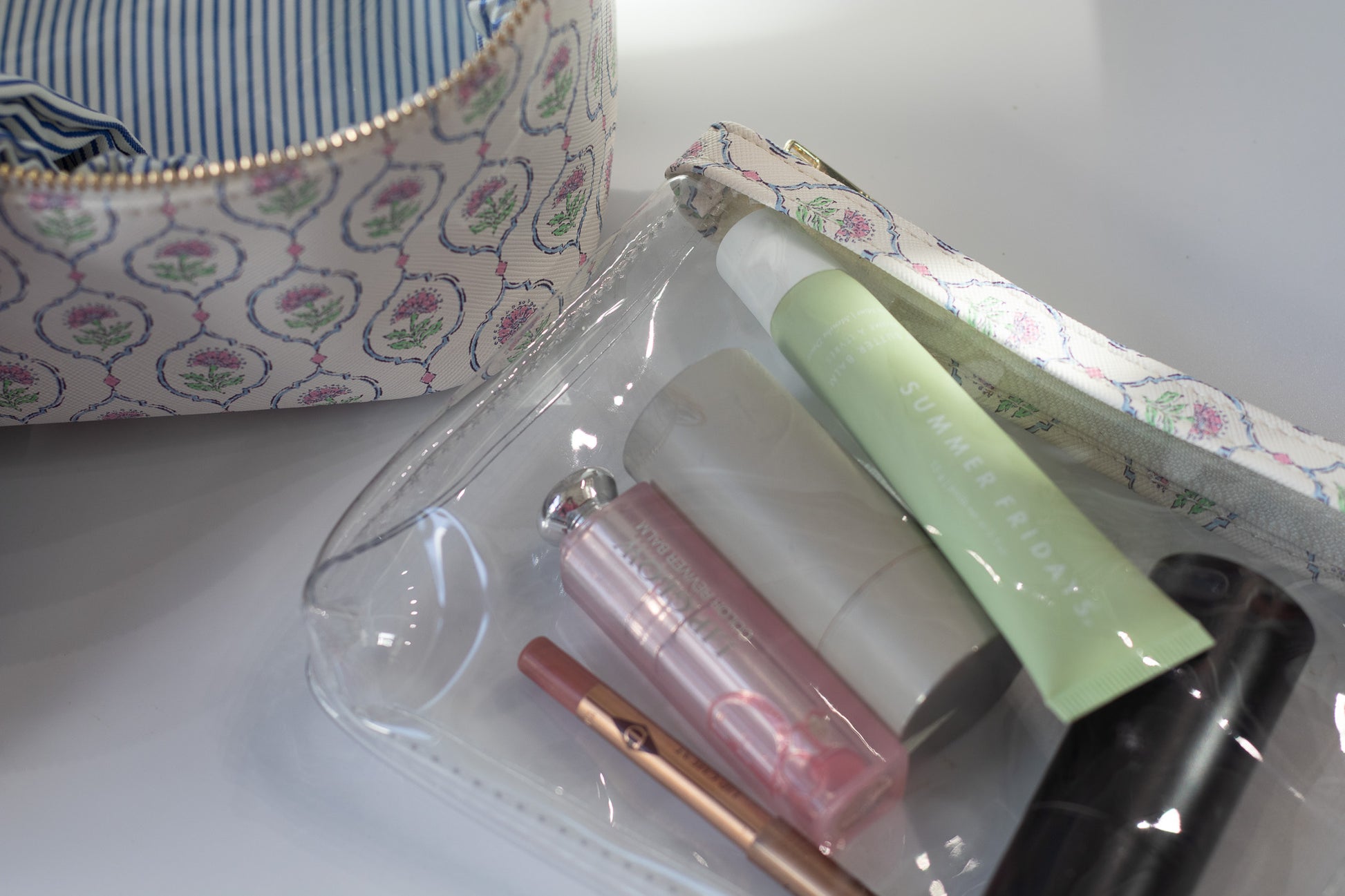 Makeup items including a lip gloss, nail file, and other small accessories in a clear pouch with a floral-patterned case.