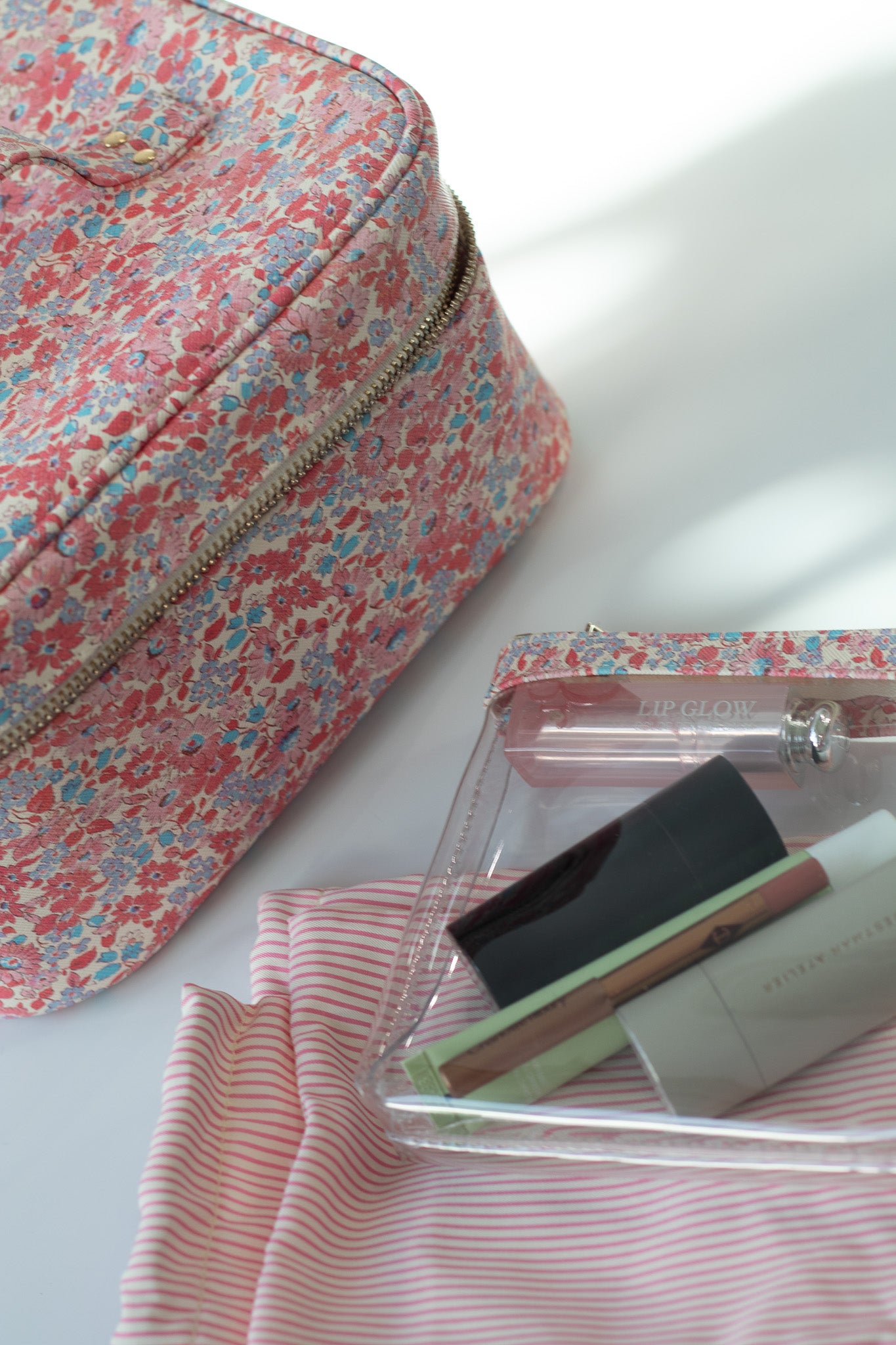 Floral makeup bag and clear case with makeup items on a white surface